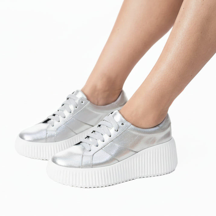 Silver sneakers worn with Christmas decorations on a white background