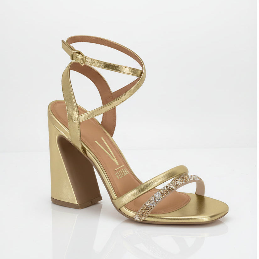 A gold-colored strappy sandal with a chunky heel and embellishments on the strap.