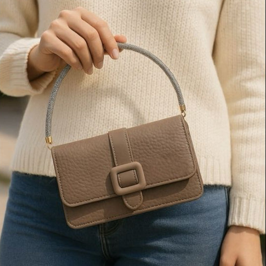 Brown handbag held by a person wearing a beige sweater and blue jeans, with a blurred background.