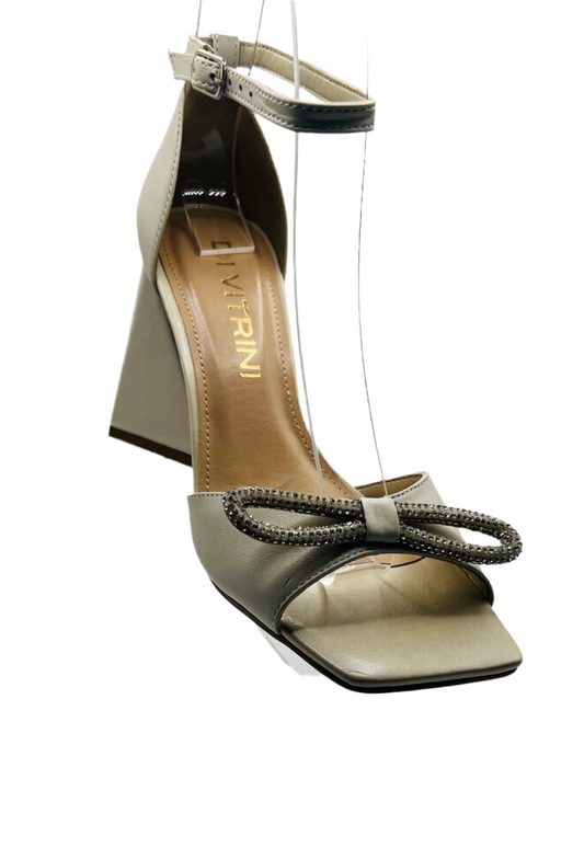 An off white sandal with a bow detail on the toe strap and an ankle strap.
